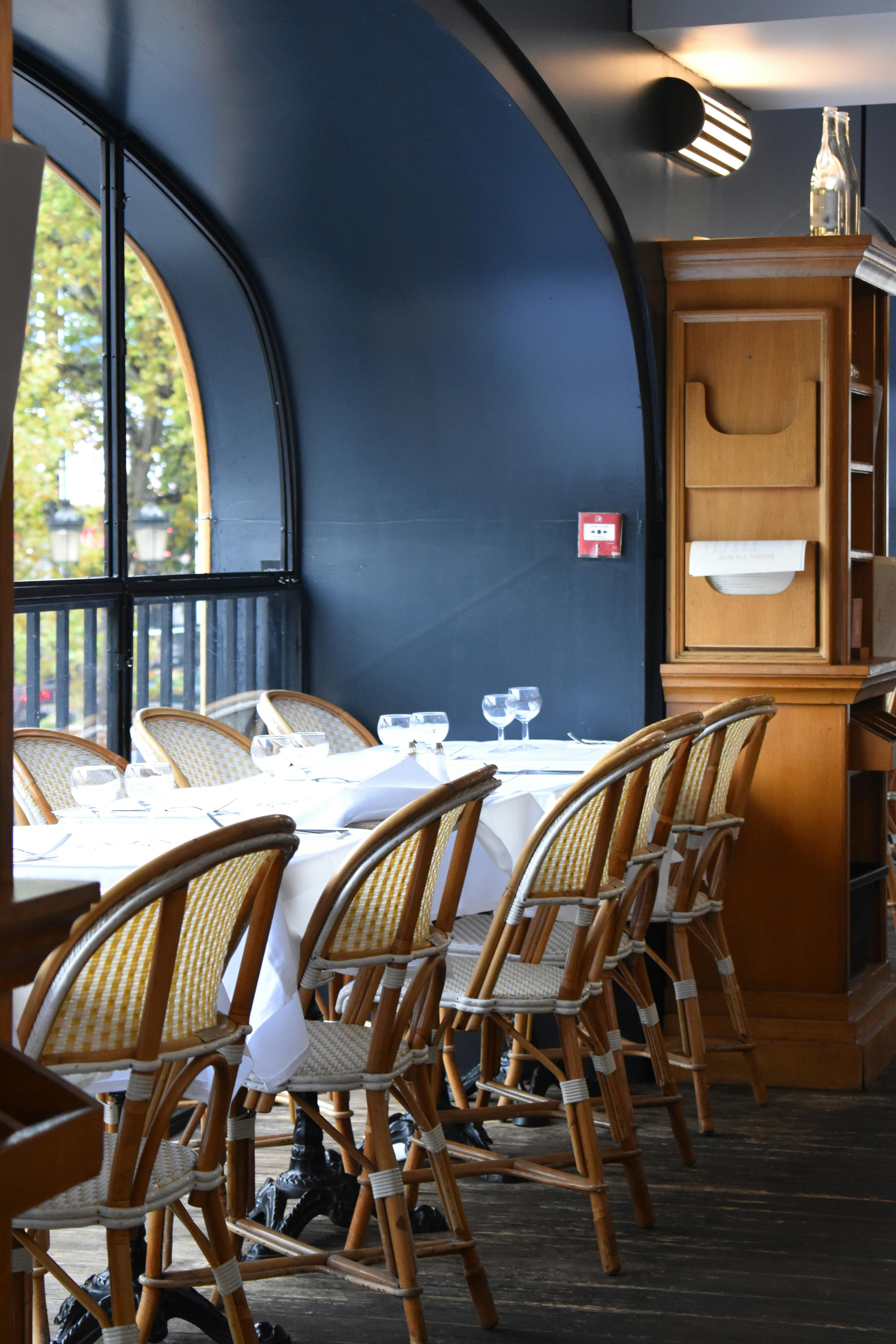 Salle de restaurant avec tables en bois, chaises et lumière matinale filtrant par les fenêtres