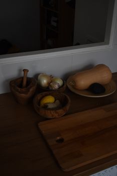 Cozy kitchen scene with fresh vegetables, wooden mortar, and chopping board.