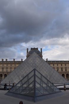 A photo of the Louvre Museum pyramid in Paris under an overcast sky.