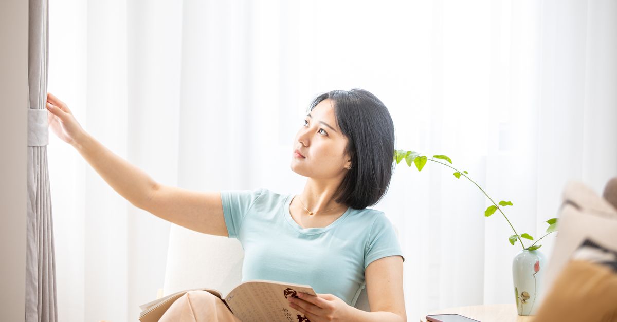 Woman relaxing in a sunlit modern living room with a book and coffee, calm aesthetic