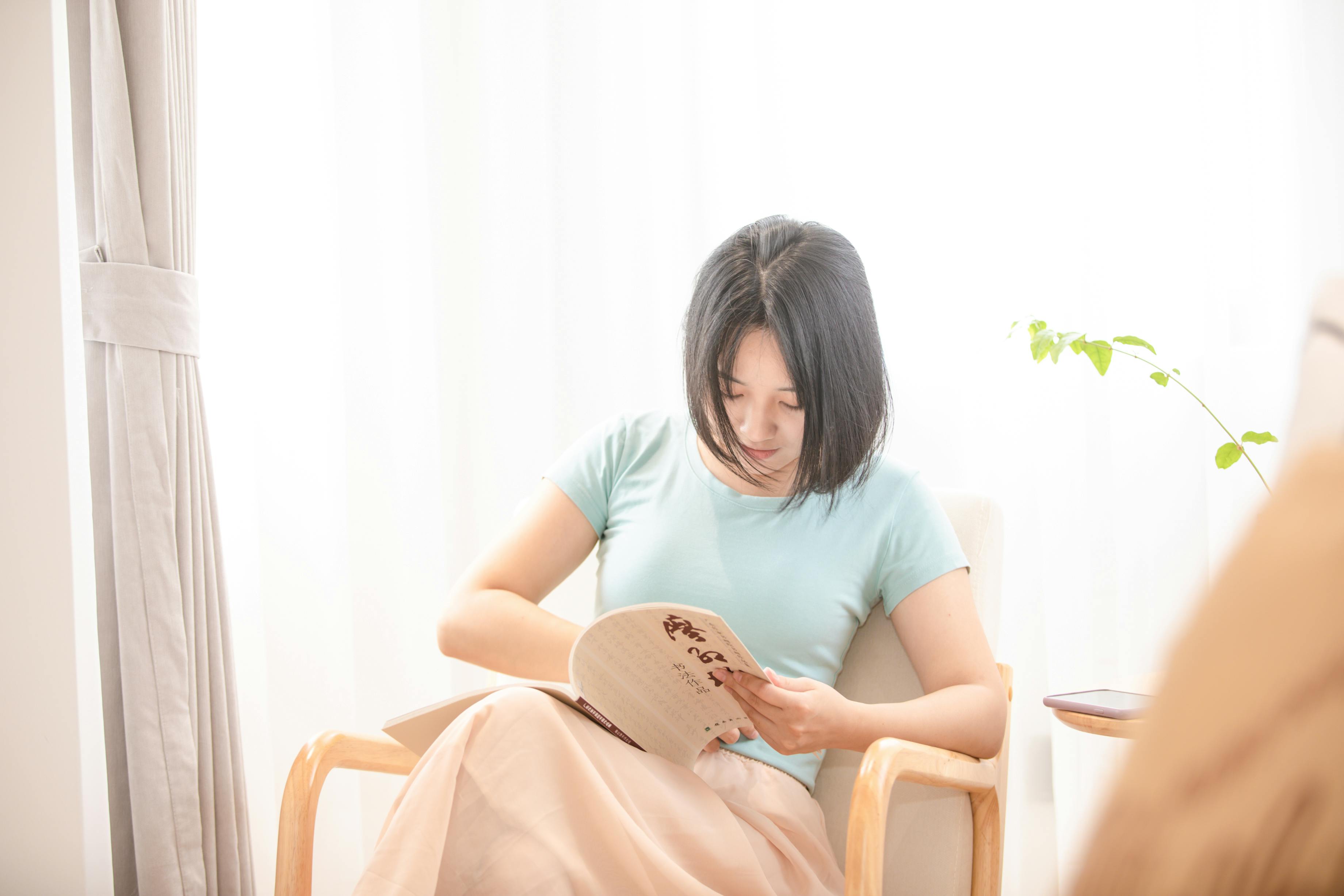 person reading a physical book in a cozy chair with natural light
