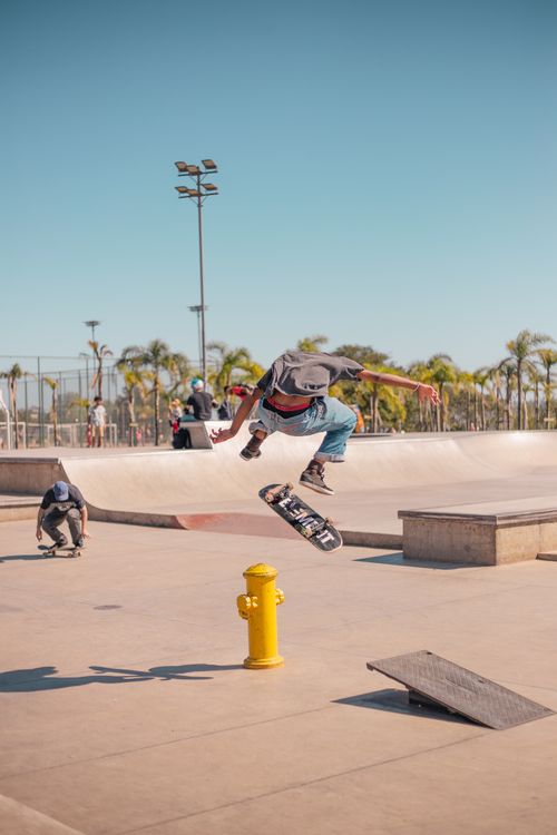 Free Skateboarder performs a trick midair at a sunny skate park, capturing dynamic motion and urban style. Stock Photo
