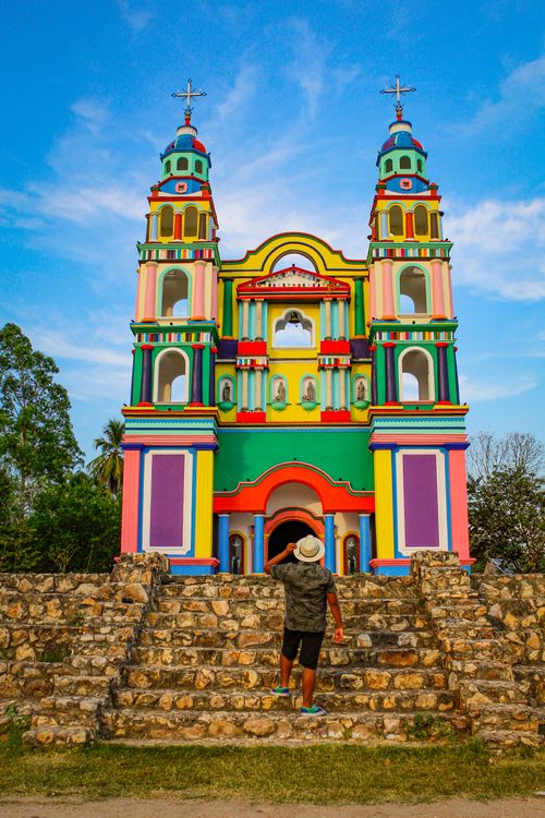 Free A person approaches a brightly colored church facade under a clear sky. Stock Photo