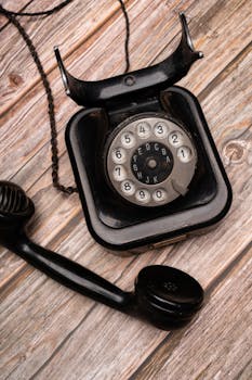 Classic black rotary dial phone on rustic wooden background. Vintage communication technology.