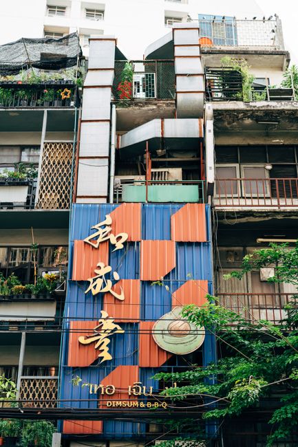 Low-angle view of an urban residential building with intricate balconies and vibrant signage.