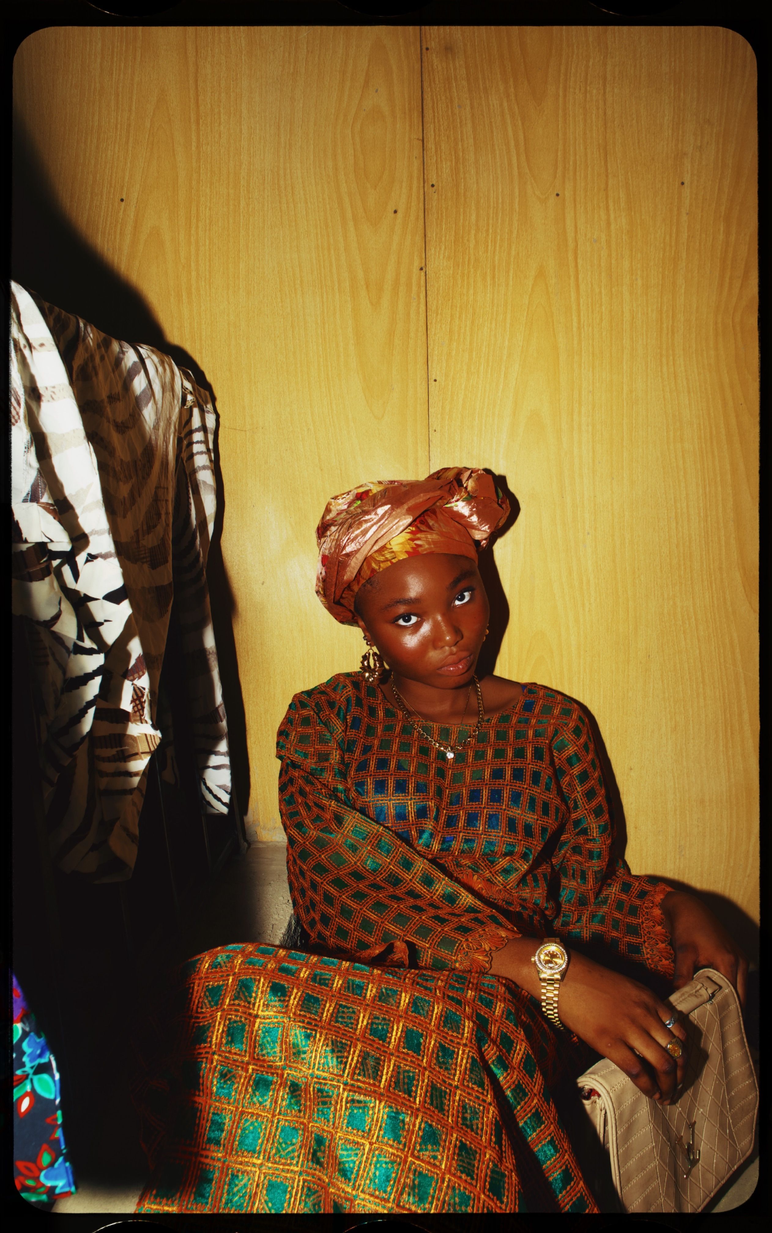 Portrait of a young woman in vibrant traditional African dress and headwrap, sitting indoors.