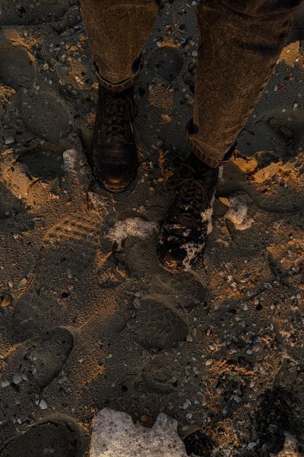 Close-up of feet walking on a sandy beach at sunset, showcasing footprints and rugged shoes.