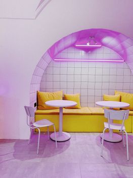 Modern cafe nook with neon lighting and bright yellow cushions, creating a stylish and inviting interior design.