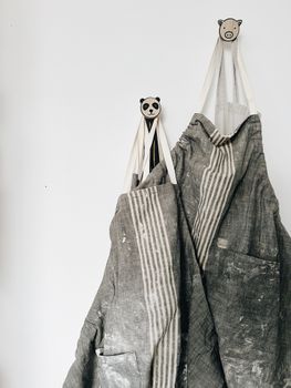 Two grey aprons with stripes hanging from panda and bear hooks on a white wall.