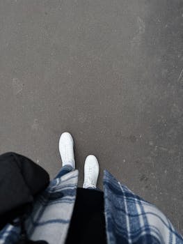 Top view of person wearing jeans and white sneakers on a city street.