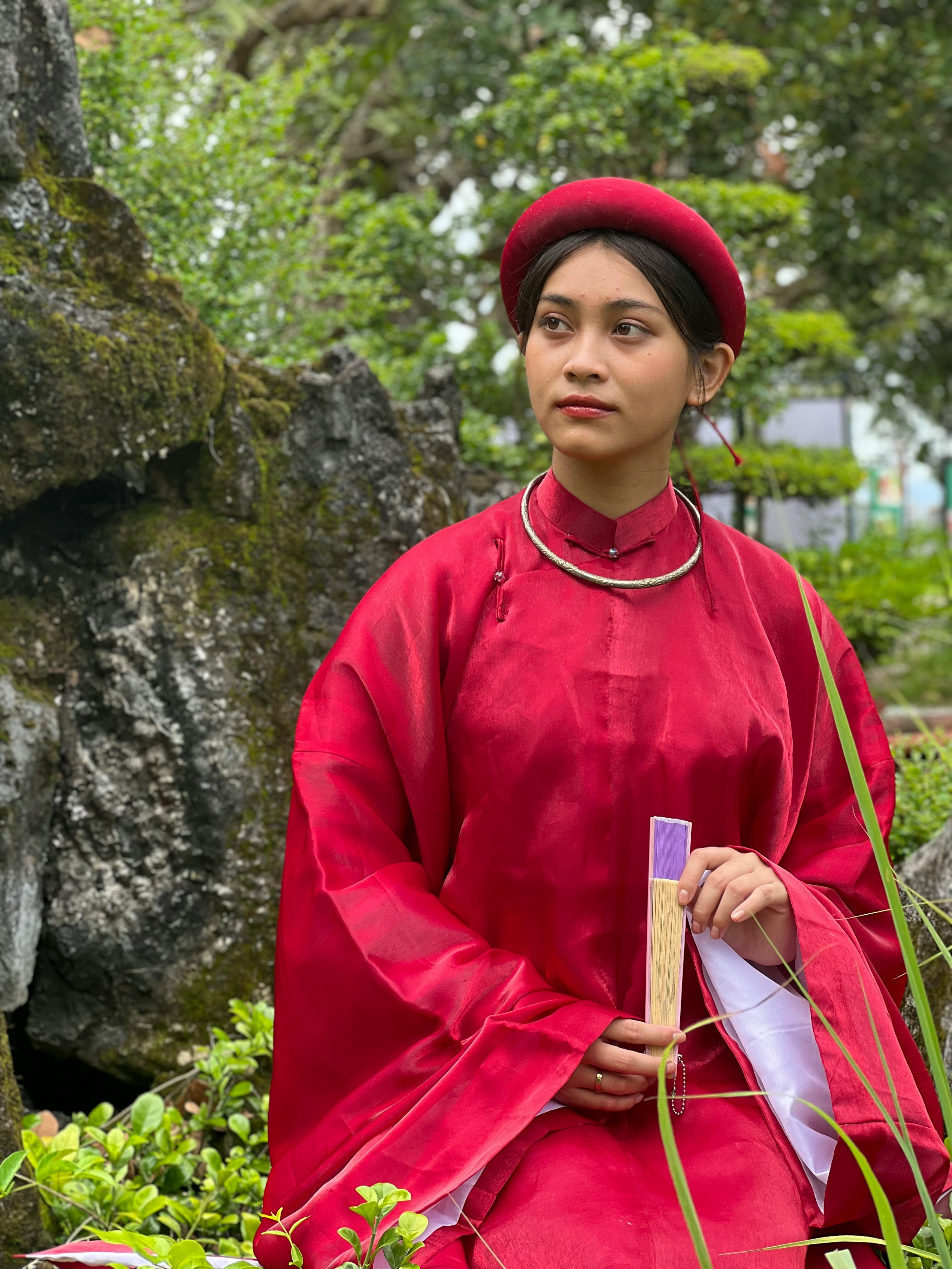 Woman dressed in traditional red hanfu poses in a lush Vietnamese park, exuding elegance.