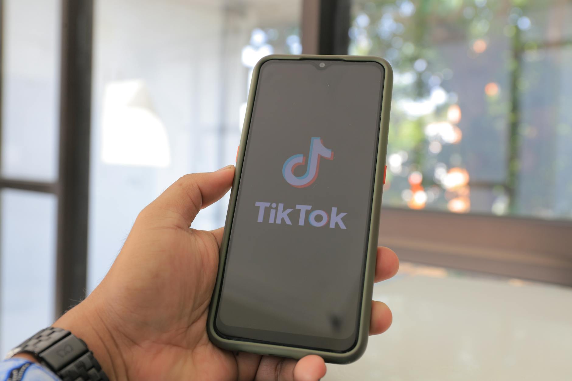 Close-up of a hand holding a smartphone with the TikTok app on screen in a bright indoor setting.