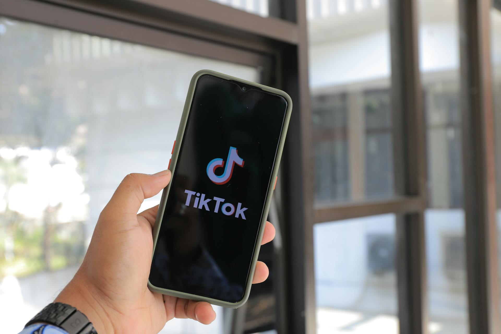 Close-up of a hand holding a smartphone displaying the TikTok app indoors.