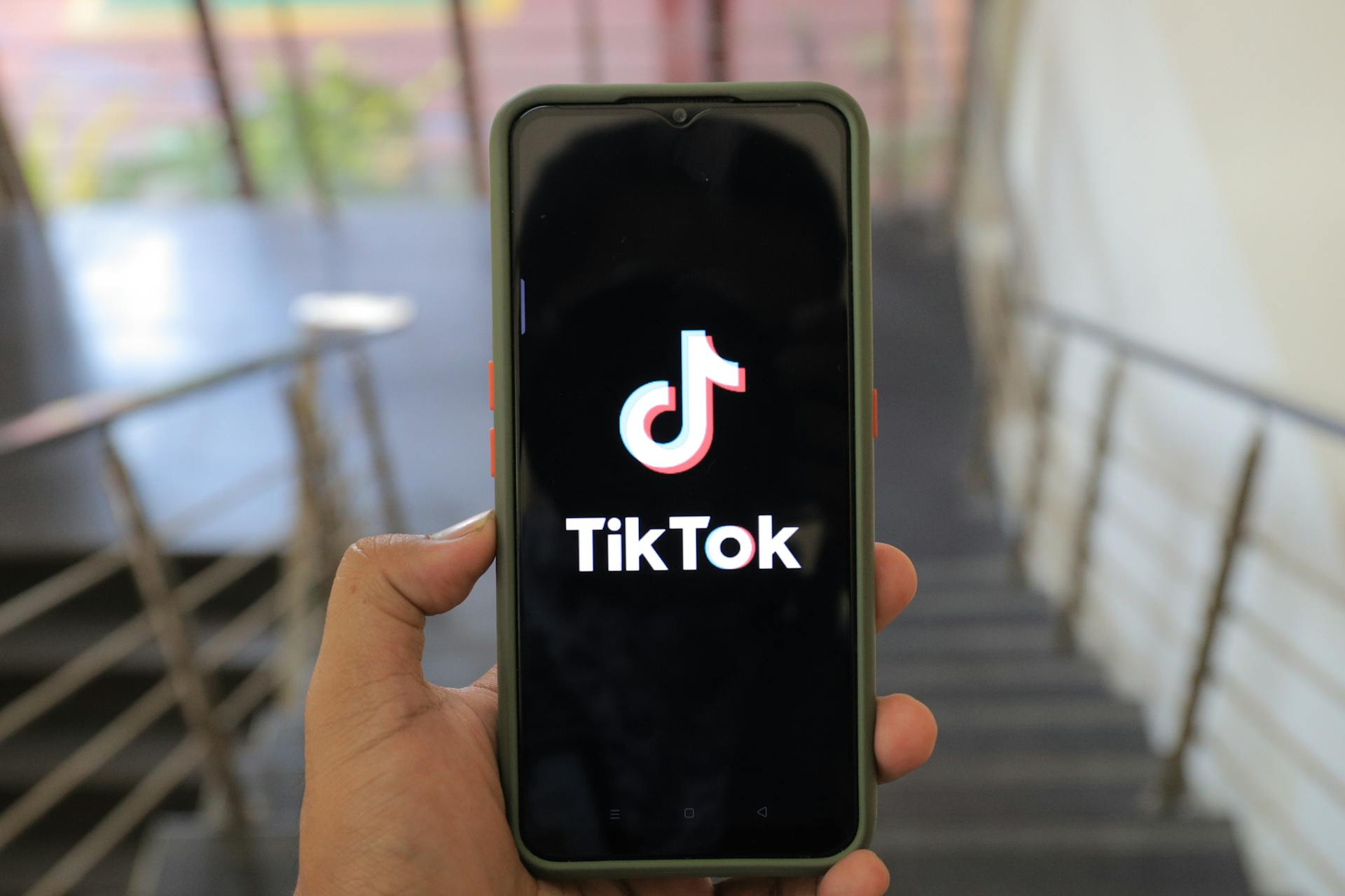 A close-up of a hand holding a smartphone displaying the TikTok app inside a modern building.