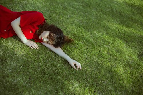Free A woman in a red dress lies on sunlit green grass, conveying stillness and solitude. Stock Photo