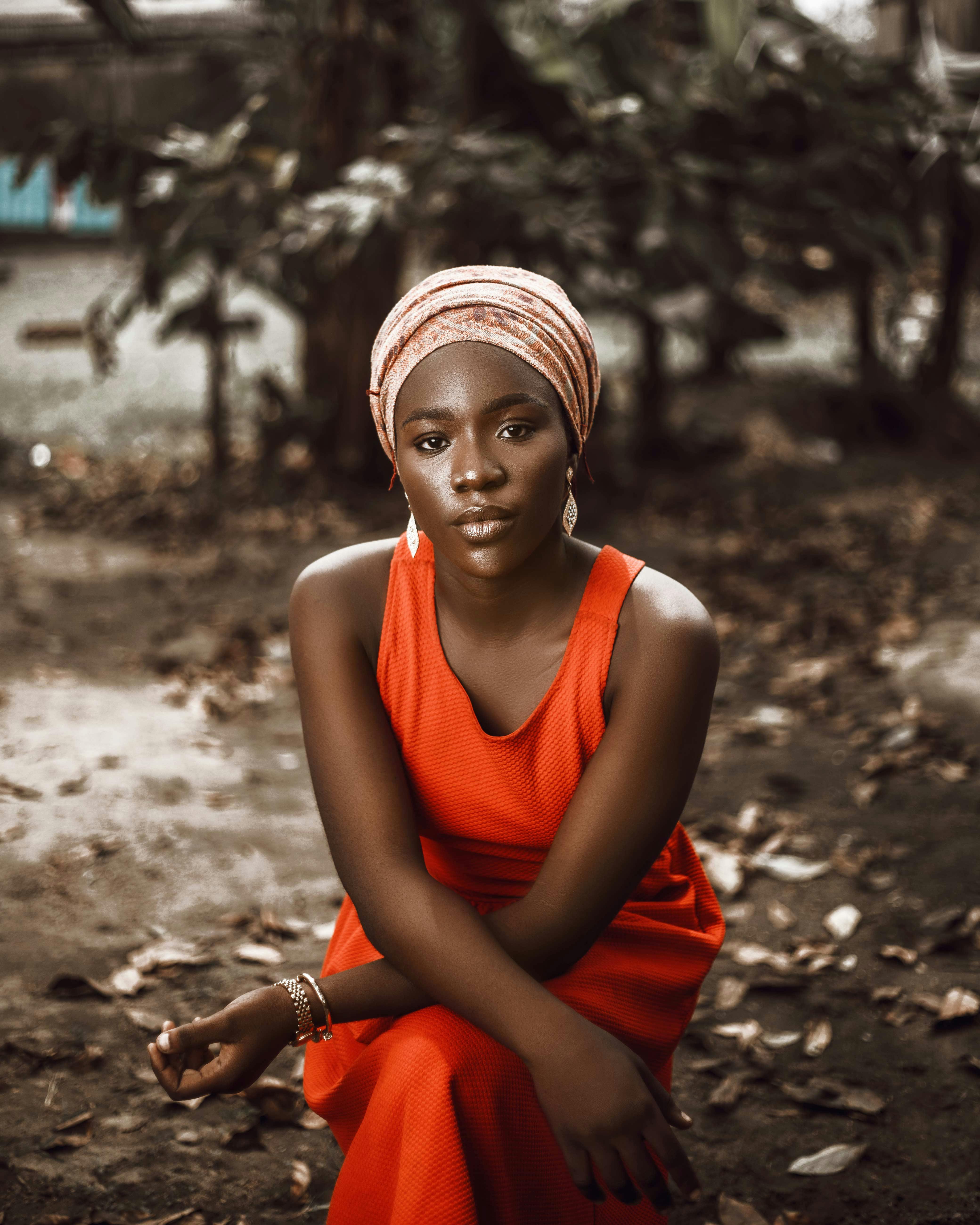 A striking portrait of an African woman in a vibrant red dress sitting outdoors, exuding grace.