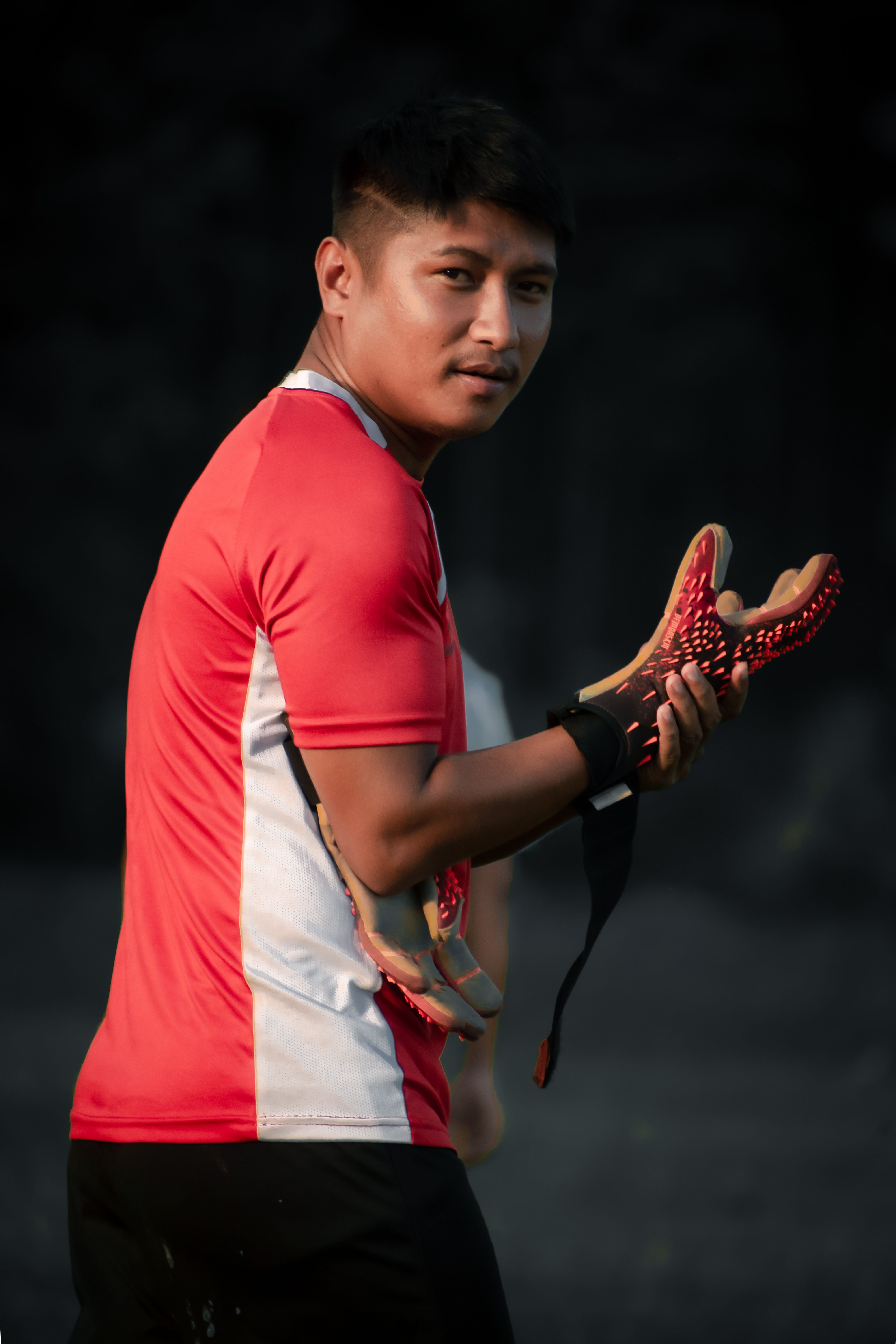 Young athlete holding sports gloves, looking back confidently in a sports field.