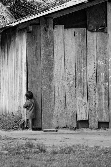 A young child stands in front of a rustic wooden wall in Mapiripán, Colombia, captured in black and white.