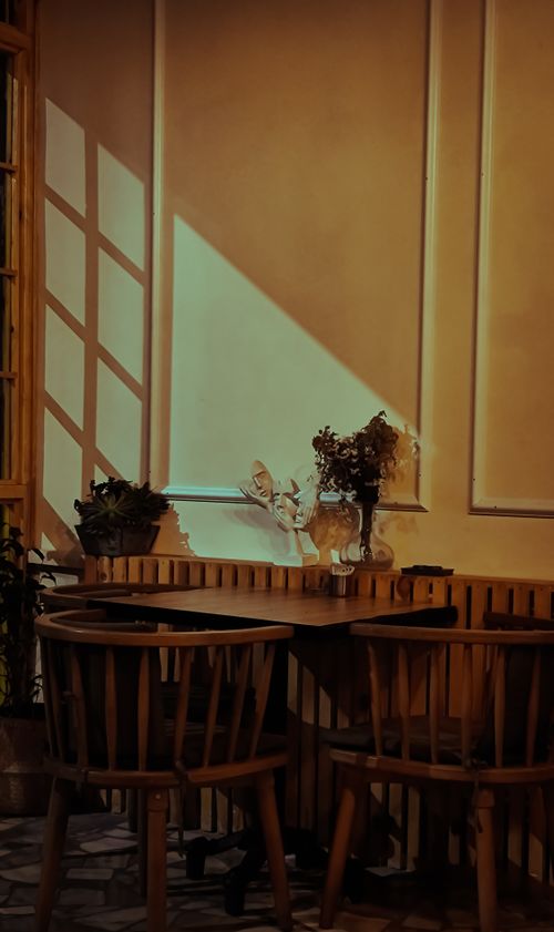 Free Warm-toned café with sunlight, wooden chairs, and potted plants creating a cozy atmosphere. Stock Photo