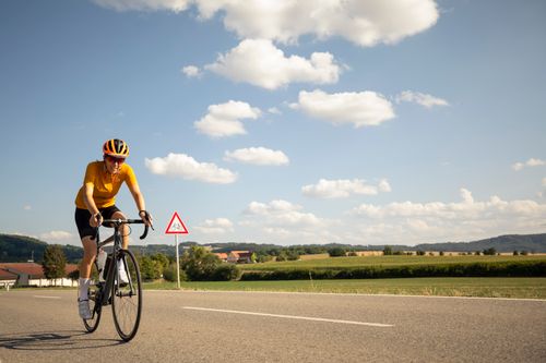 Free A cyclist in yellow rides a road bike on a sunny day with a beautiful countryside backdrop. Stock Photo