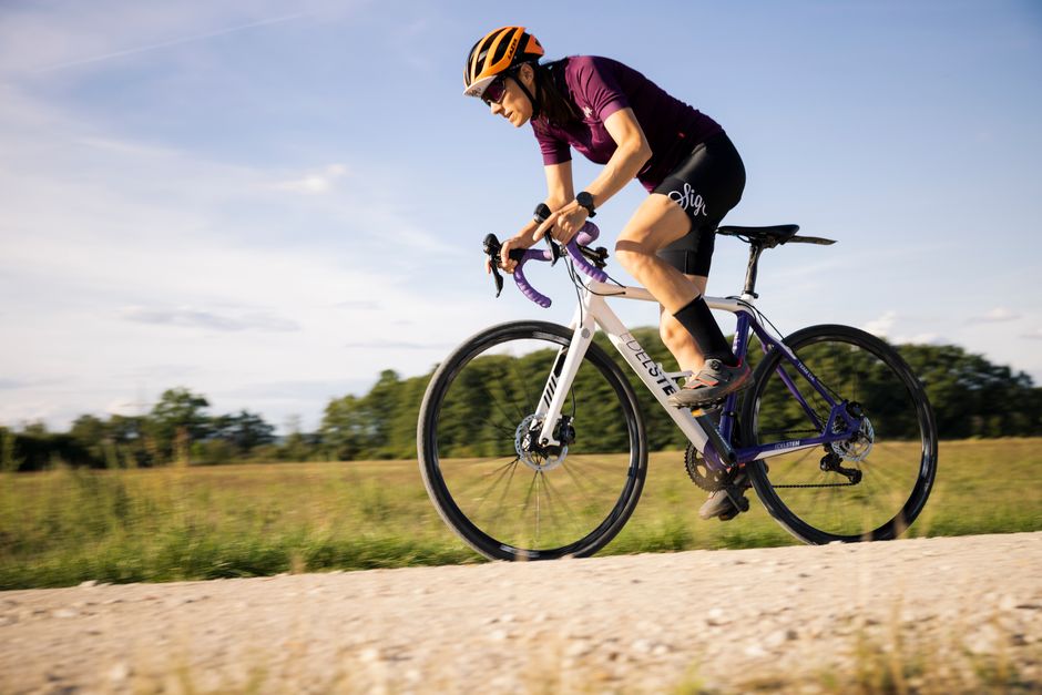 Cyclist wearing helmet rides a road bike on a sunny day in open countryside.