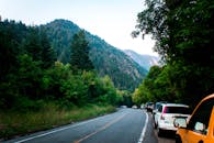 晴空下，蜿蜒的山路边停着汽车，绿树成荫