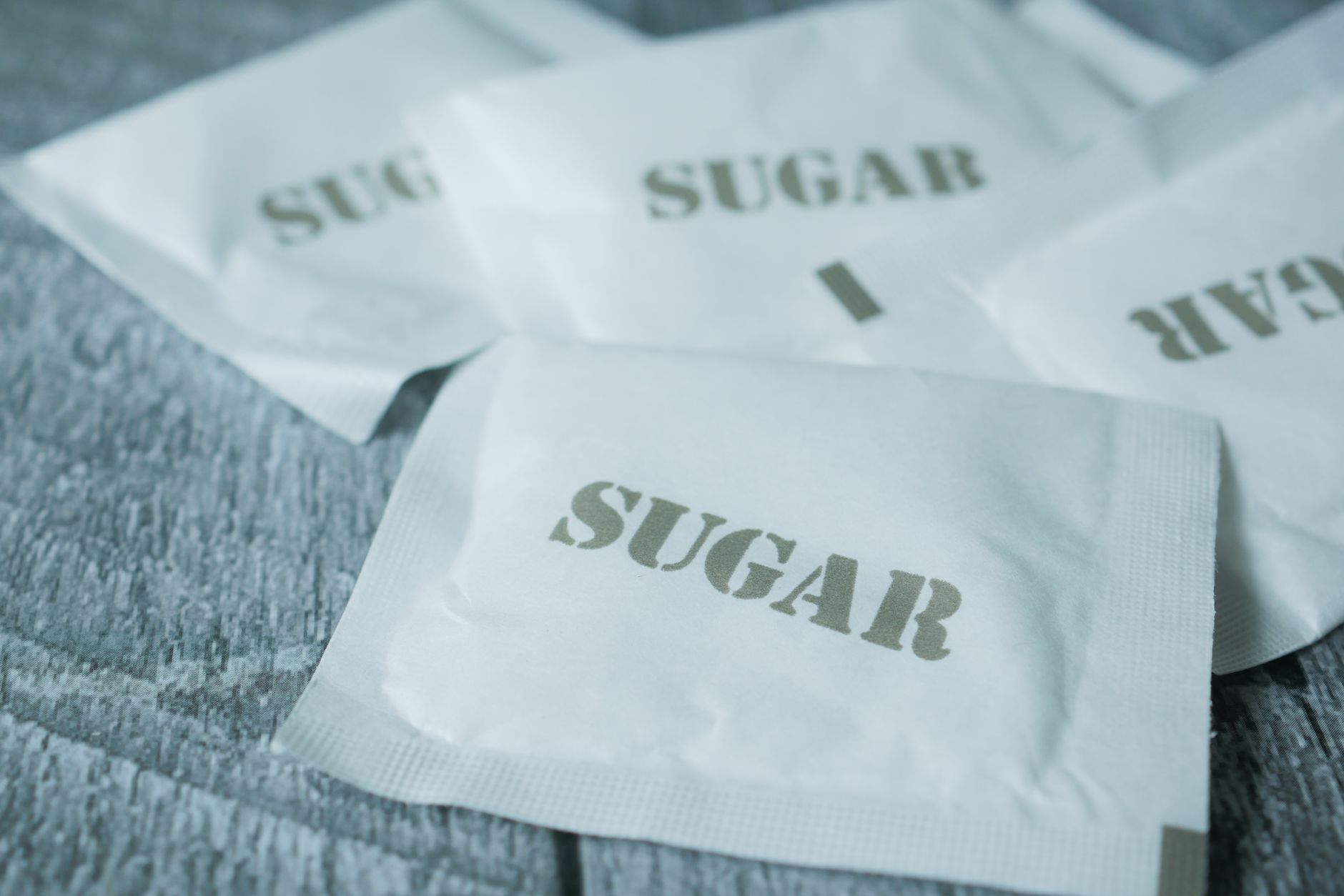A detailed view of white sugar packets scattered on a rustic wooden surface.