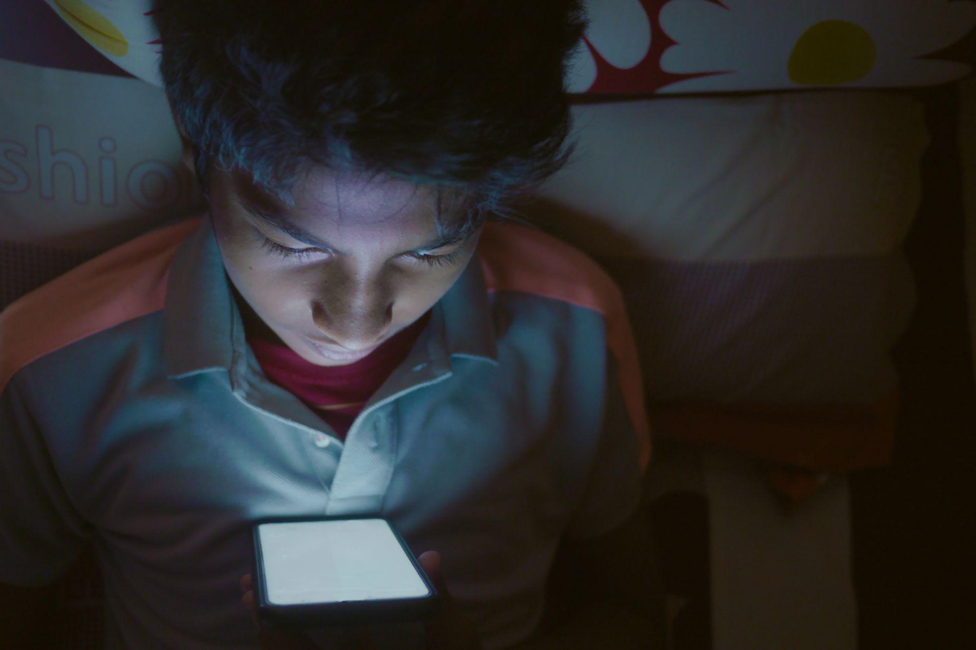 Adolescente observa un teléfono celular dentro de una habitación con poca luz