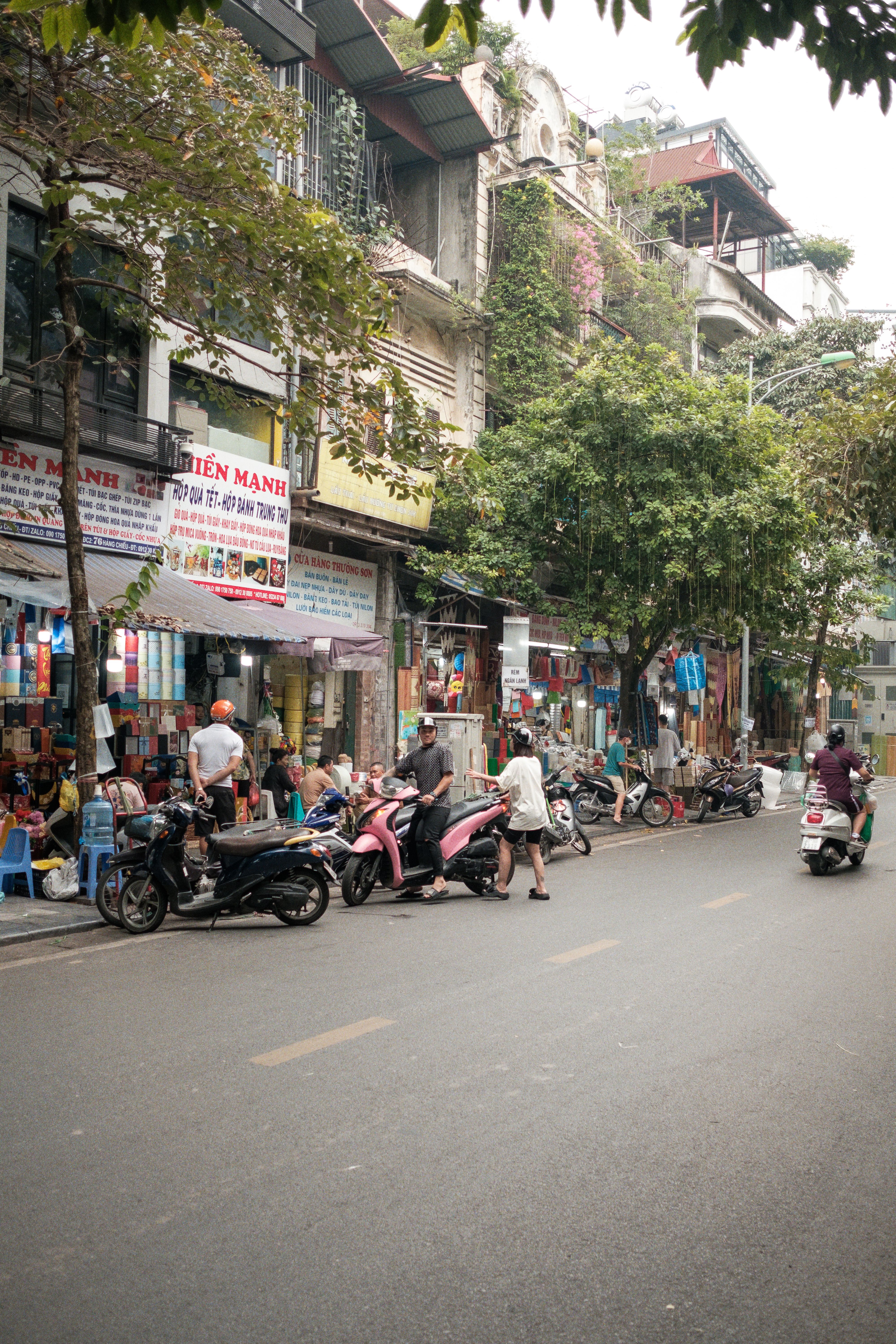 Vibrant street life in Hanoi, showcasing local shops, motorbikes, and pedestrians. Perfect for travel and culture themes.