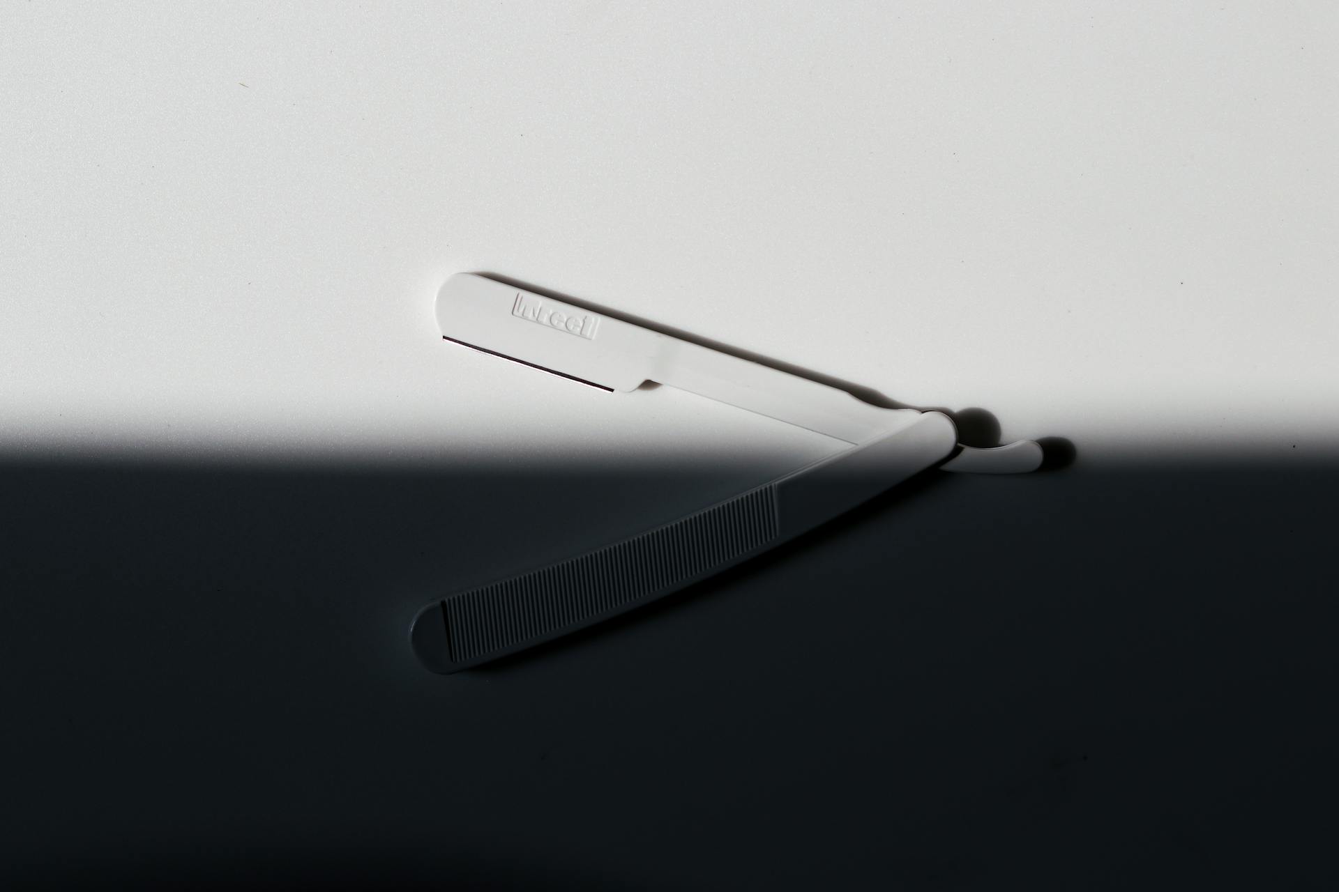 Elegant black and white photo of a razor blade casting a shadow on a white surface.