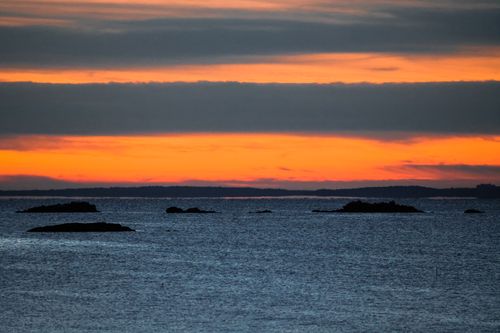 Free Captivating ocean landscape with vibrant orange sunrise and silhouetted rocky formations. Stock Photo