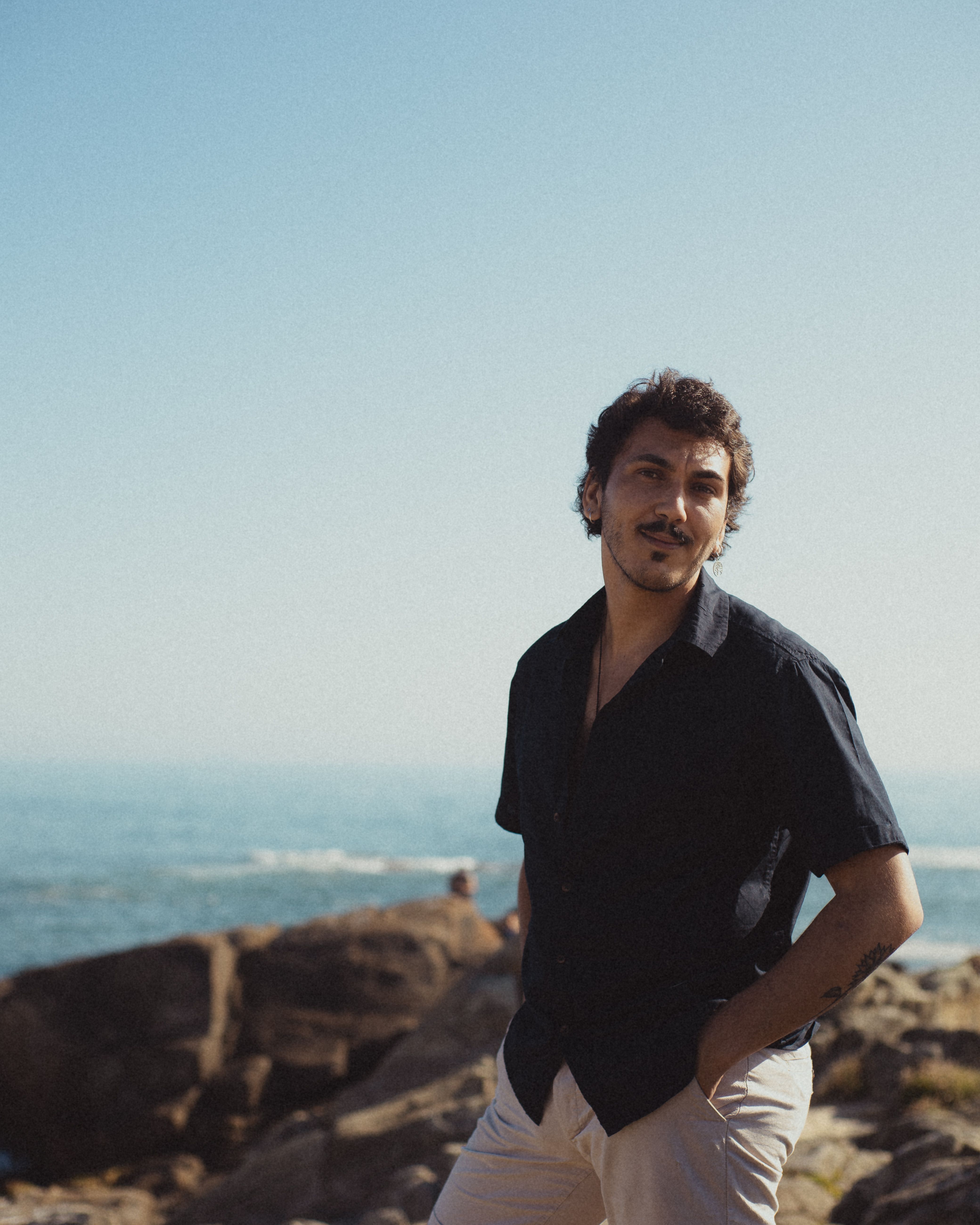 Portrait of a fashionable man standing on rocky seaside, exuding a casual and confident vibe.