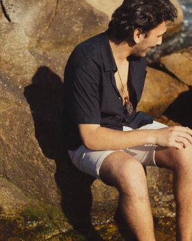 A man in casual summer attire relaxes by the sea on a sunny day. Perfect for travel and lifestyle themes.