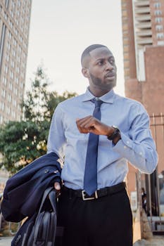 Stylish businessman checking watch as he walks through a downtown area, holding his suit jacket.