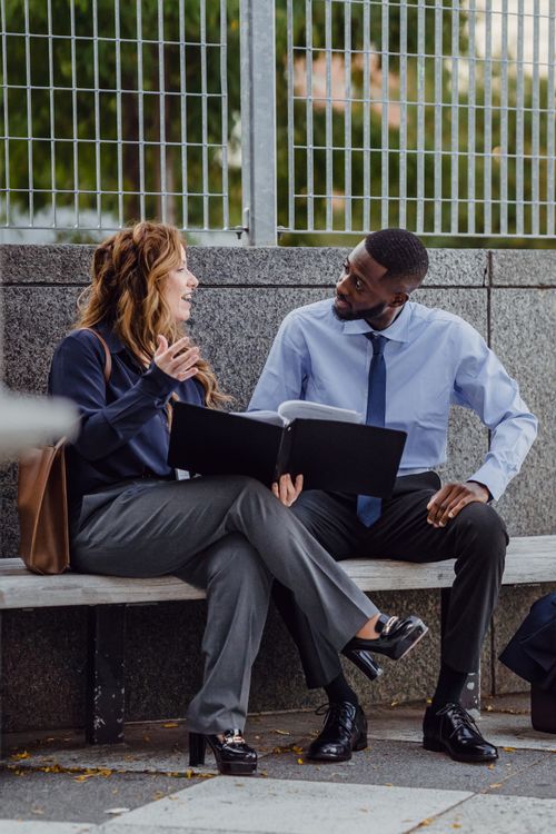 Free Two business professionals discuss documents outdoors, enhancing collaboration. Stock Photo