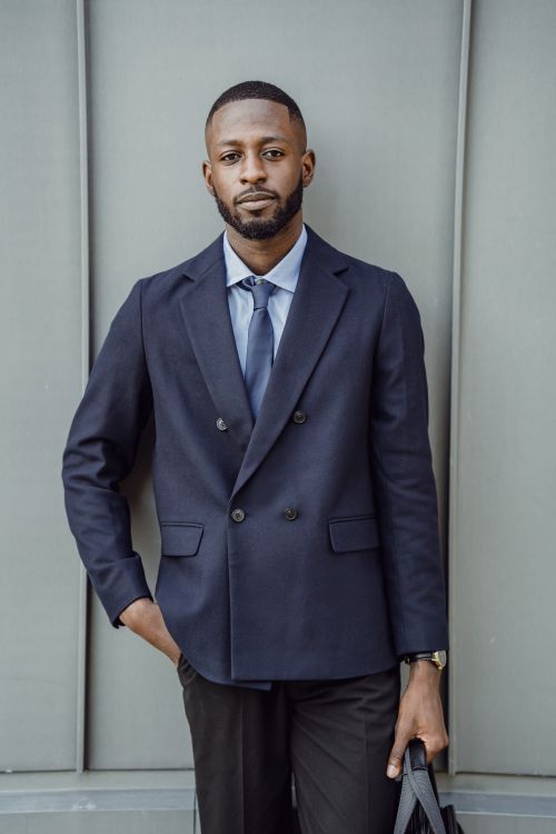 Free African American businessman in a navy suit posing confidently outdoors against a modern backdrop. Stock Photo