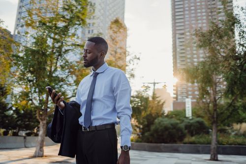 Free A businessman outdoors in an urban park checks his smartphone during sunset. Stock Photo