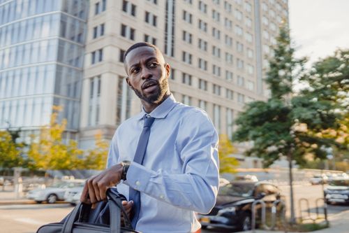 Free Businessman outdoors in urban setting, carrying a bag, looking serious and professional. Stock Photo