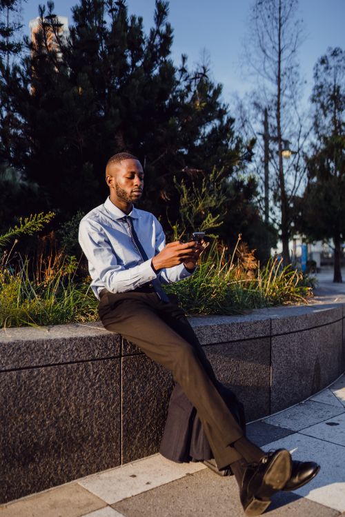 Free African American man in suit using smartphone outdoors in urban setting during day. Stock Photo