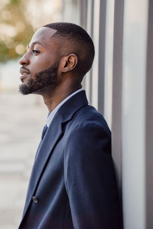 Free Elegant side profile shot of a man in a suit leaning against a wall outdoors. Stock Photo