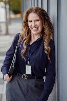 A smiling businesswoman poses confidently against a wall outdoors, showcasing professional attire.