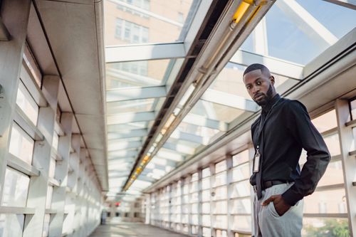 Free A fashionable man poses confidently in a modern glass corridor with urban architecture. Stock Photo