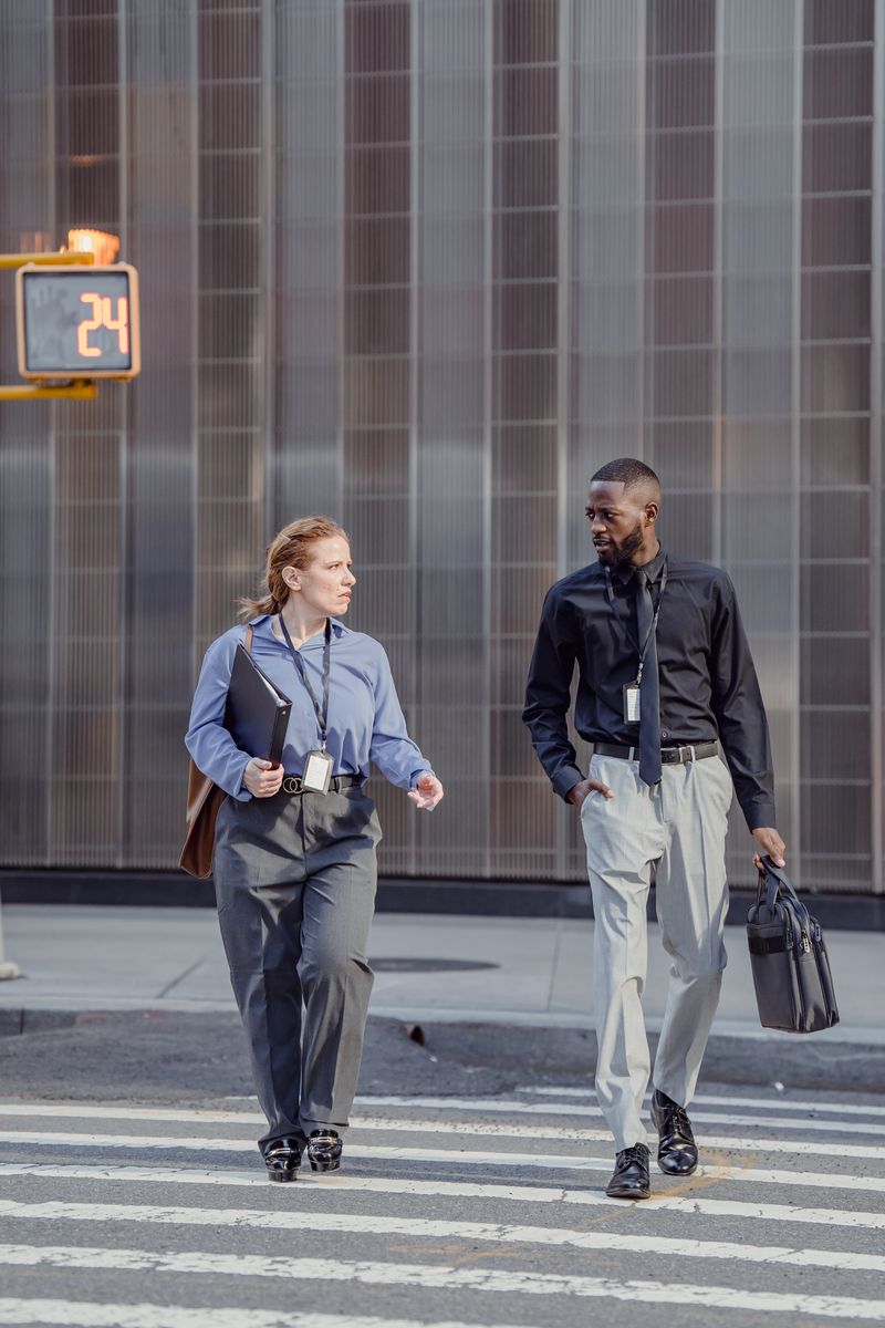 Two professionals cross a city street with briefcases
