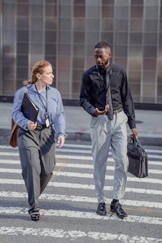 Two business professionals conversing while crossing a city street.