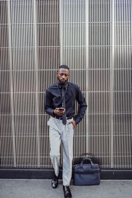 Free Man in fashionable attire using a smartphone in an urban setting. Modern and stylish. Stock Photo