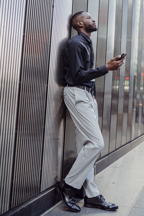 Free Stylish man standing with a smartphone against a textured urban backdrop. Modern lifestyle concept. Stock Photo