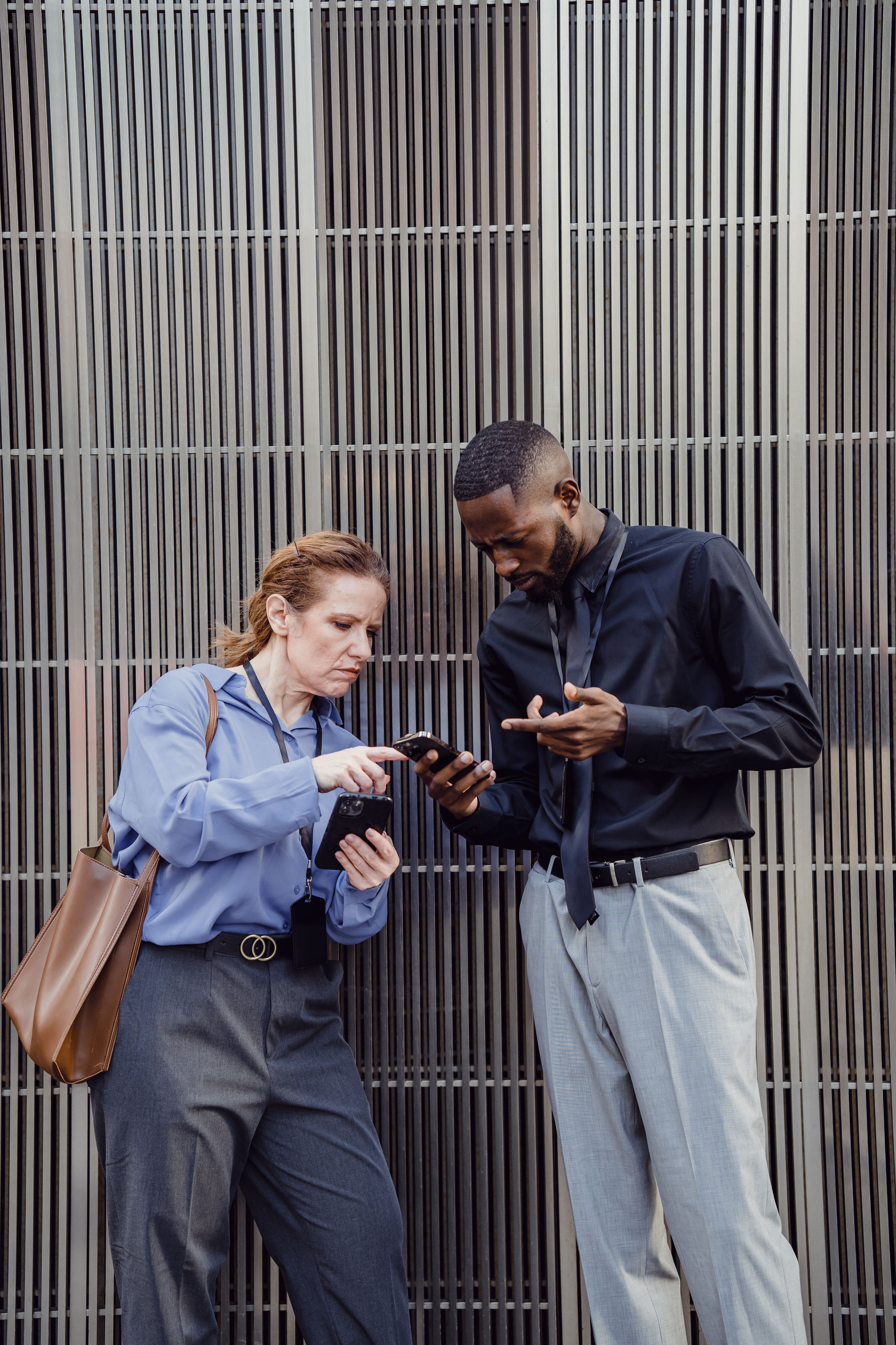 Deux professionnels consultent leur smartphone devant un bâtiment de bureaux