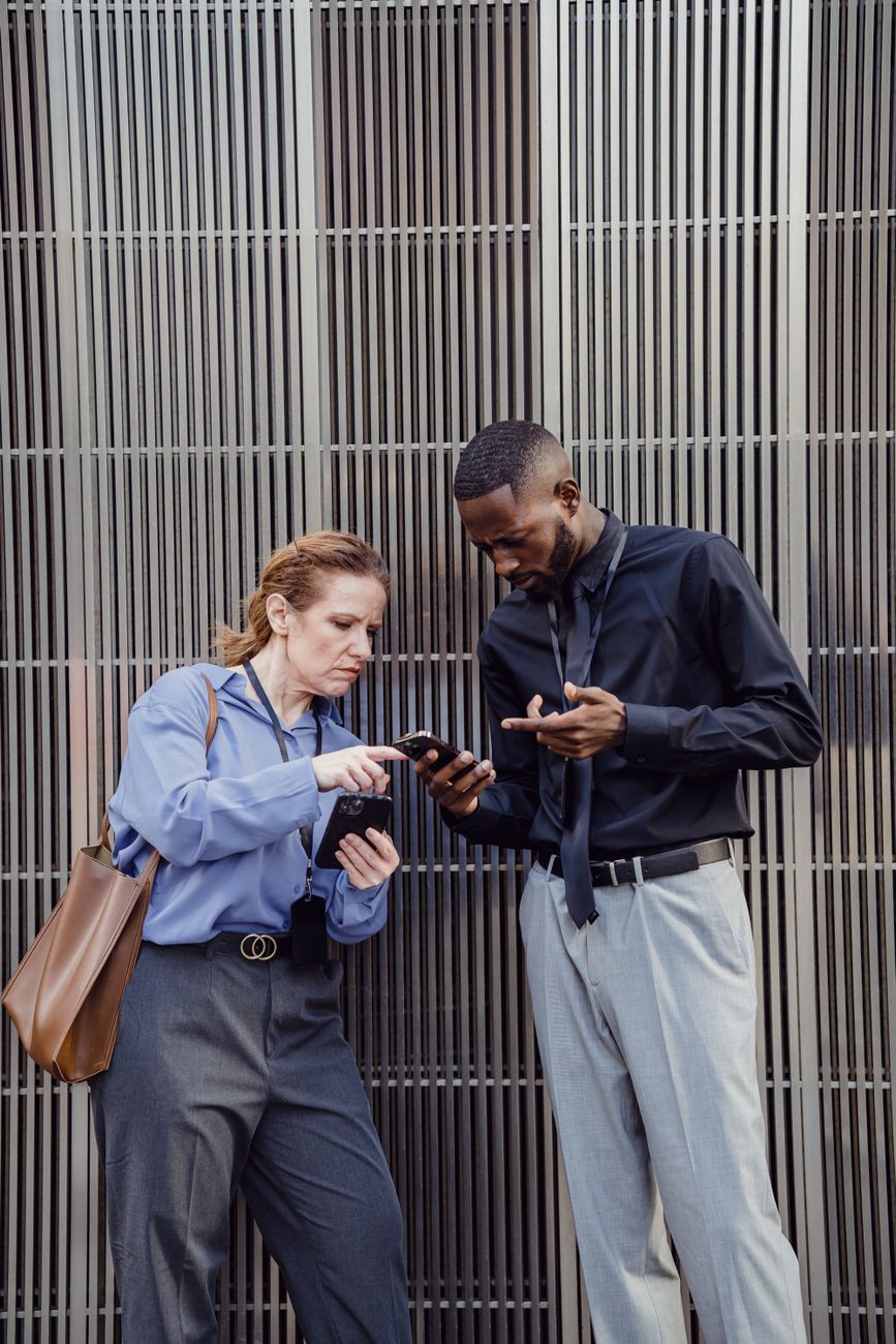Deux professionnels consultent leur smartphone devant un bâtiment de bureaux