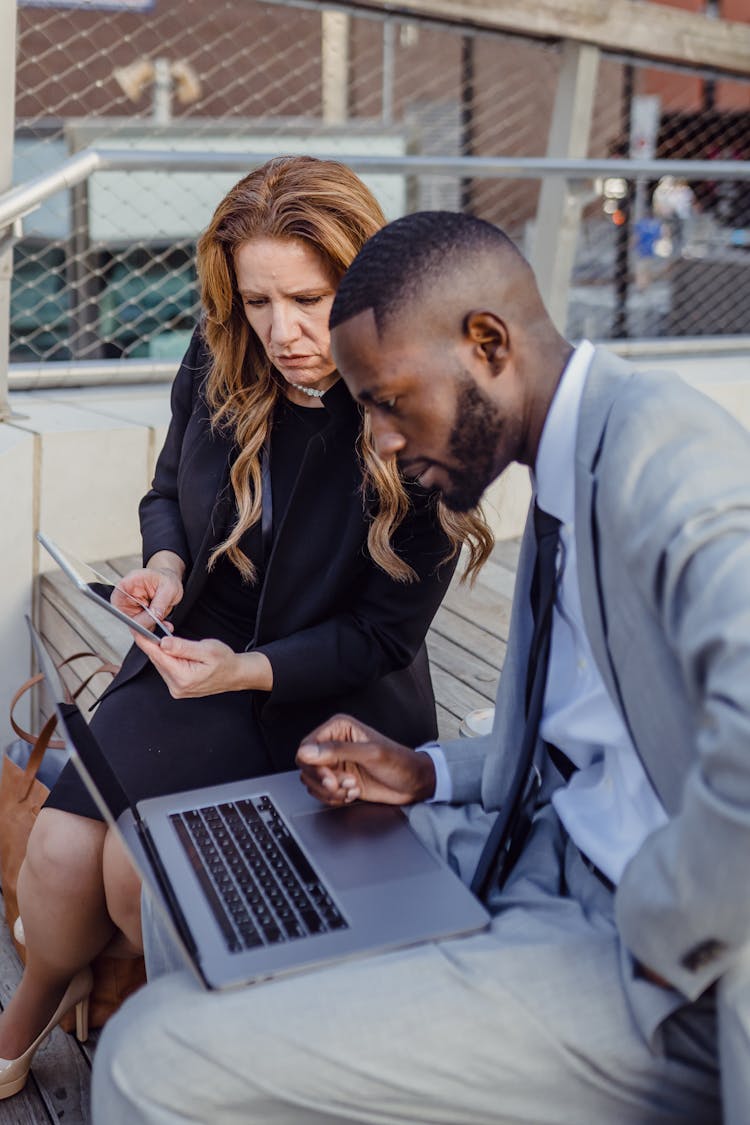 Male And Female Office Workers Using Laptop And Tablet Outdoors