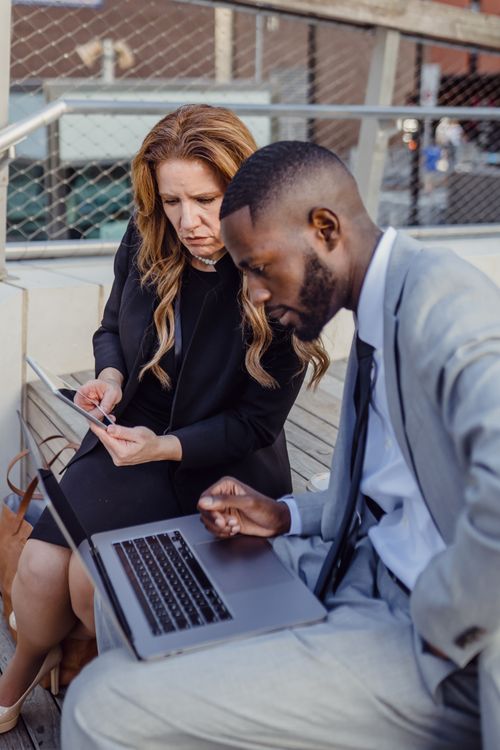 Free Business professionals collaborate using laptop and digital tablet outdoors. Teamwork and strategy in focus. Stock Photo